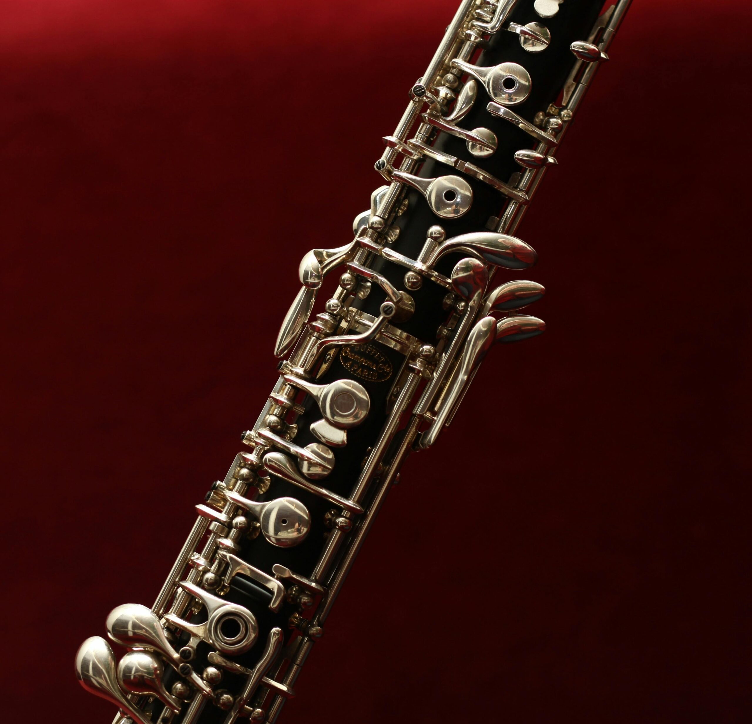 Biography Detailed close-up of an oboe with intricate keys set against a rich red background, highlighting its elegance.