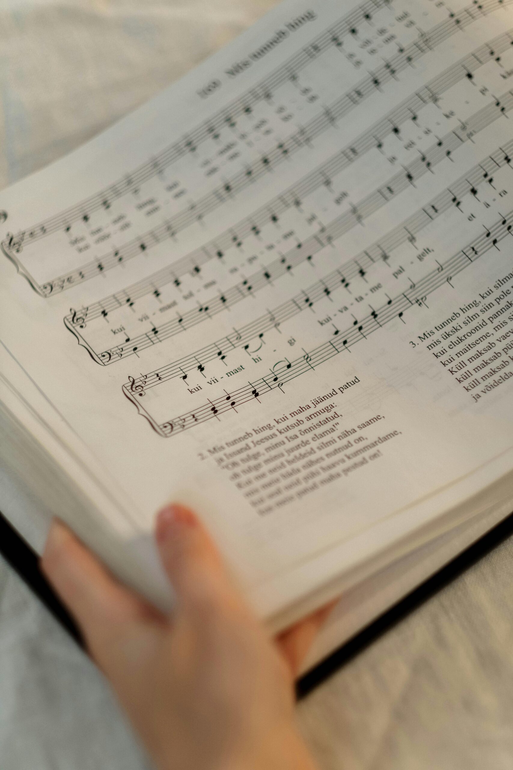Biography Close-up view of a hand holding open sheet music with musical notation.